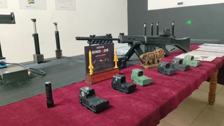Holographic weapon sights displayed on a table beside a rifle.